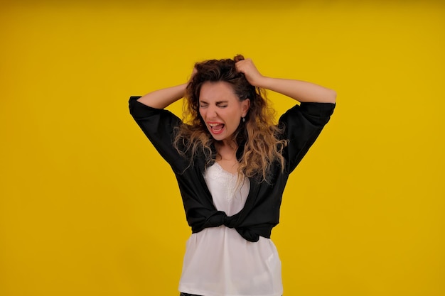 Closeup portrait of a beautiful girl on a yellow background woman screaming and holding her hair human emotions