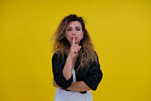 Closeup portrait beautiful girl on a yellow background woman showing finger silence girl showing shh sign keep secret