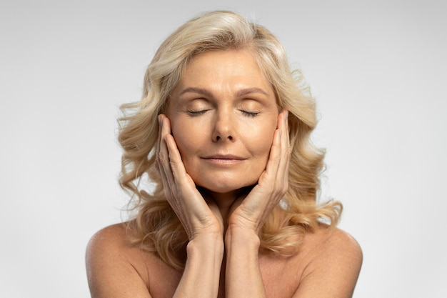 Closeup portrait of beautiful mature with eyes closed touching face isolated on background