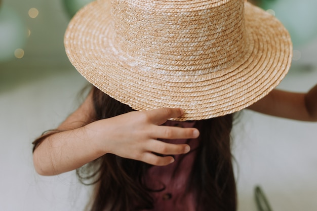 Closeup portrait of a beautiful smiling little girl with dark hair in a straw hat