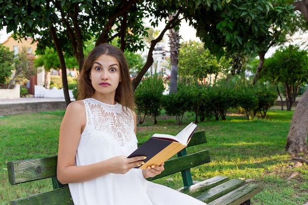 Closeup portrait of a beautiful surprised girl with wide opened eyes while reading a book 