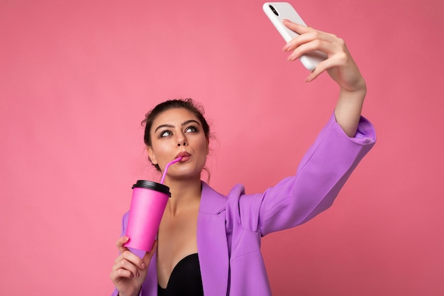 Closeup portrait of a beautiful young brunet woman in fashionable purple suit on a pink background