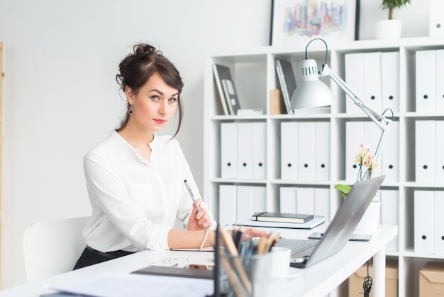 Closeup portrait of a businesswoman at her workplace working with pc looking in camera wearing office suit