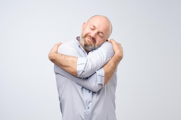 Closeup portrait of confident smiling man holding hugging himself isolated on grey wall background Love yourself concept