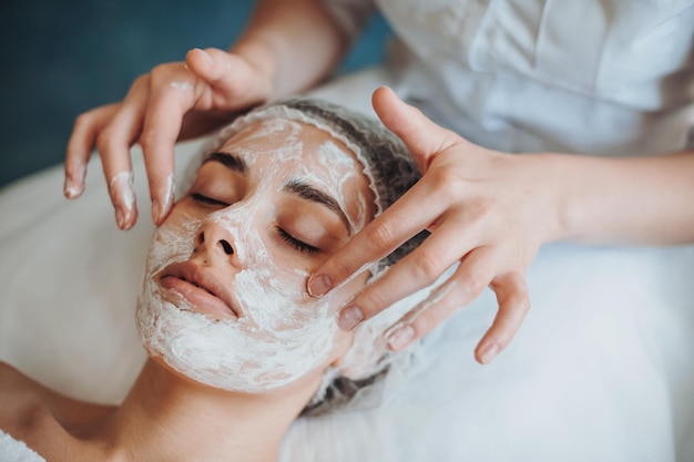 Closeup portrait of cosmetologists hands applying mask on clients face in spa salon natural beauty f...