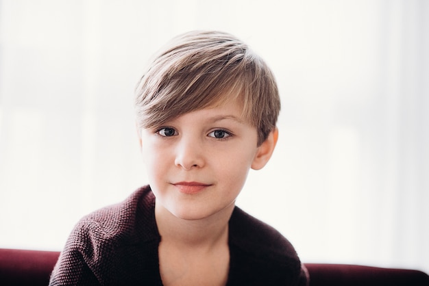 A closeup portrait of a cute boy kid sitting on a sofa against the light window soft focus