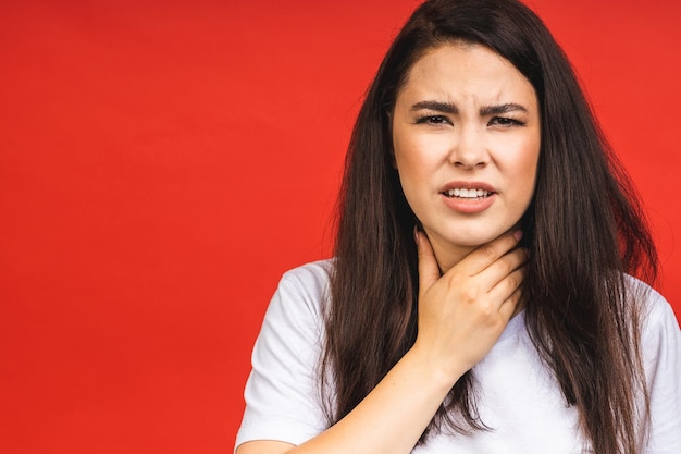 Closeup portrait of cute sick young brunette woman in casual having sore throat holding hand on her neckThroat pain painful swallowing concept Inflammation of the upper respiratory tract