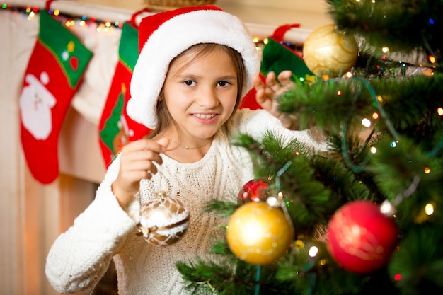 Closeup portrait of cute smiling girl decorating Christmas tree with golden balls