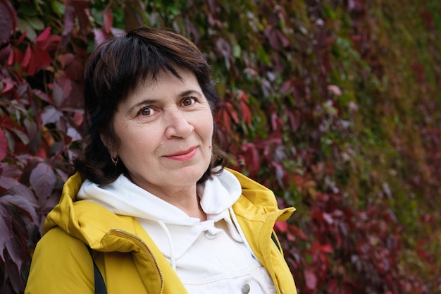 Closeup portrait of an elderly woman against a wall of red autumn vine leaves