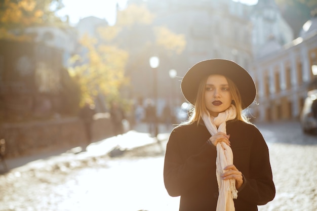 Closeup portrait of fashionable blonde model wearing hat and scarf, walks down the street. Space for text