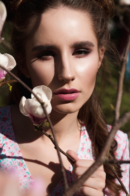 Closeup portrait of fashionable brunette woman standing near blooming magnolia flowers