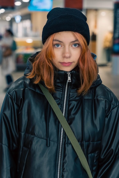 Closeup portrait of a fashionable teenage girl with striking red hair wearing a stylish black knitted hat and jacket exuding confidence and individuality