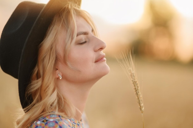 Closeup portrait of a girl in a hat in the summer at sunset in the wheat