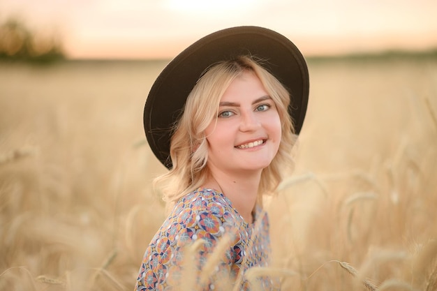 Closeup portrait of a girl in a hat in the summer at sunset in the wheat