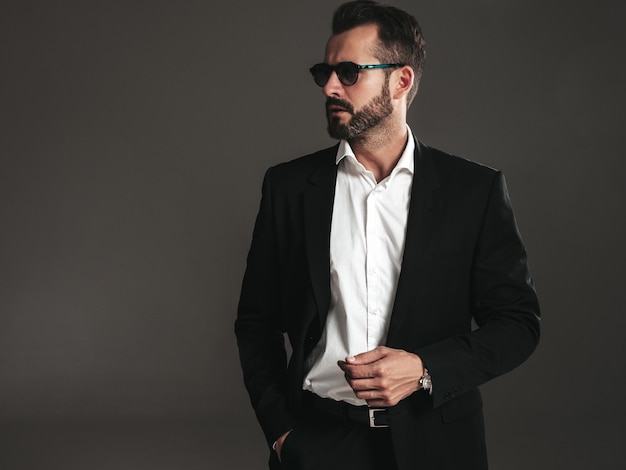 Closeup portrait of handsome confident stylish hipster lambersexual model Sexy modern man dressed in elegant black suit Fashion male posing in studio on dark background In sunglasses