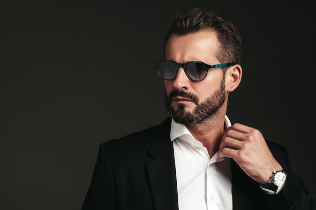 Closeup portrait of handsome confident stylish hipster lambersexual model Sexy modern man dressed in elegant black suit Fashion male posing in studio on dark background In sunglasses