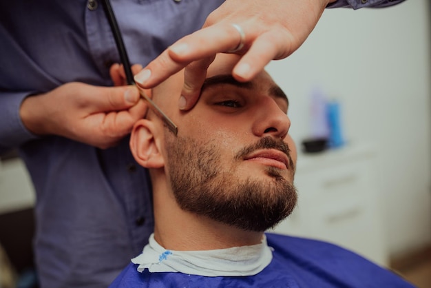 Closeup portrait of a handsome young man getting beard shaving with a straight razor