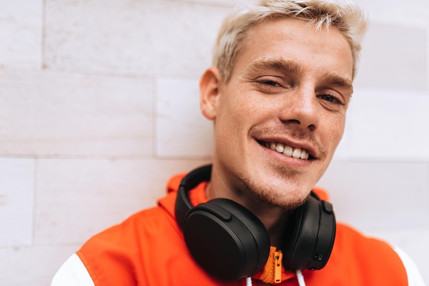 Closeup portrait of handsome young man looking at one side with headphones on the neck sitting against  light grey outdoor background Lifestyle people technology and music concept