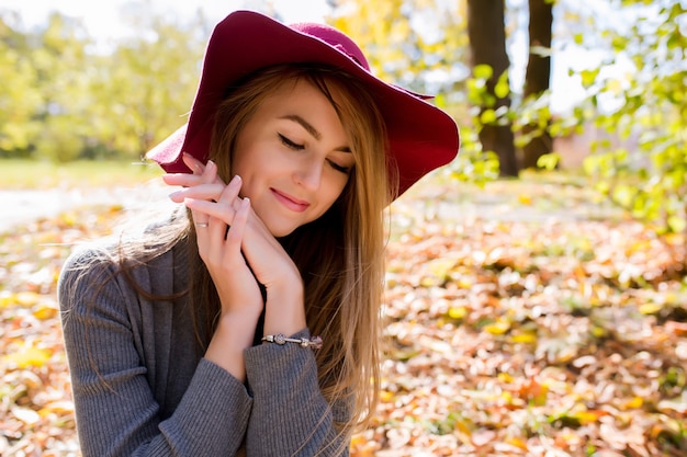 Closeup portrait of happy blonde woman with natural makeup in red hat posing at the park