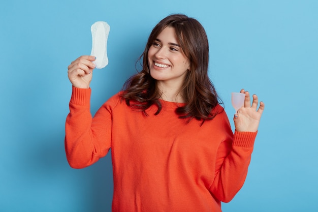 Closeup portrait of happy female with dark hair holding hygiene pad and menstrual cup