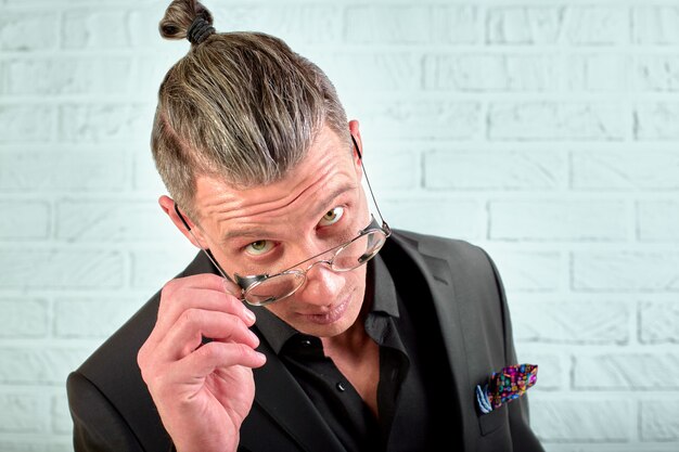 Closeup portrait of a happy young businessman with glasses looking at the camera on white wall