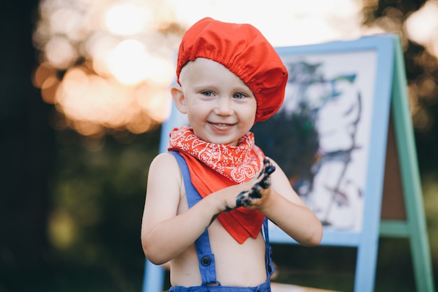 Closeup portrait of a little boy who smiles in embarrassment and rejoices in the paint in her hands