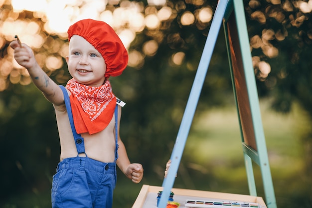 Closeup portrait of a little boy who smiles in embarrassment and rejoices in the paint in his hands at sunset