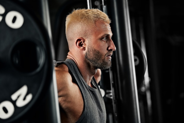 Closeup portrait of a muscular man workout with barbell at gym. Brutal bodybuilder athletic man with six pack, perfect abs, shoulders, biceps, triceps and chest.