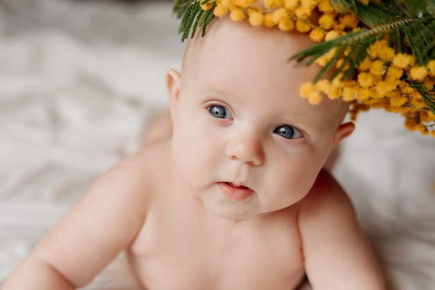 Closeup portrait of a newborn baby lying on a white bed with a sprig of mimosa