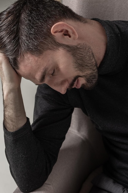 Closeup portrait of a nice and handsome brutal man sitting on the chair and looking down