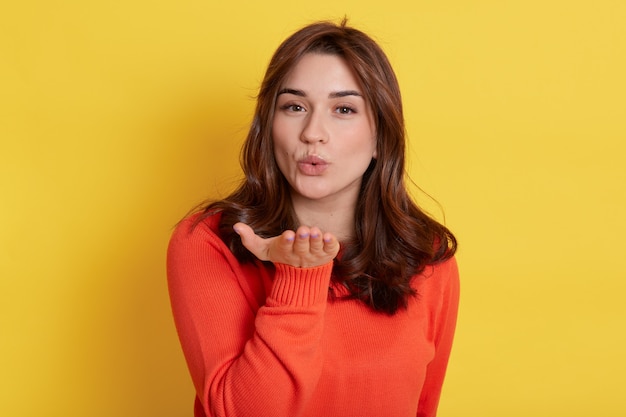 Closeup portrait of nice looking attractive lovely female, coquettish cheerful girl pouts lips sending gentle air kiss over yellow, looks at camera.