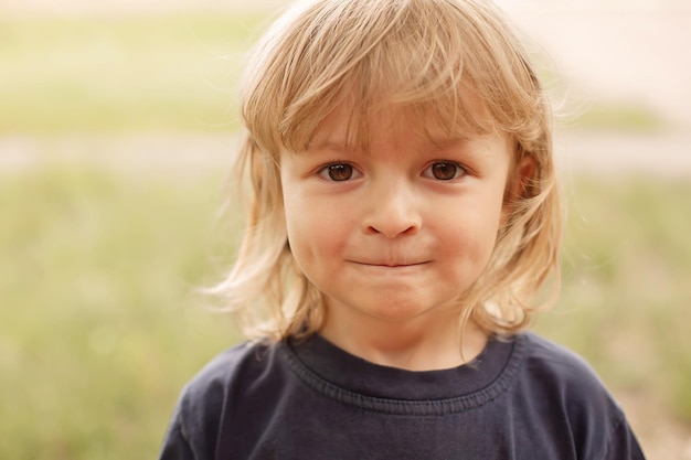 closeup portrait of the pensive face of a little blond boy on a green background summer street