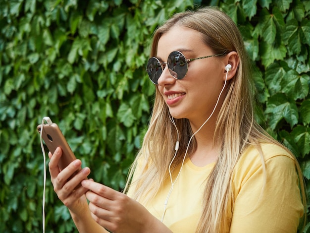 Closeup portrait of a pretty blonde woman uses a mobile phone with headphones a girl listens to musi