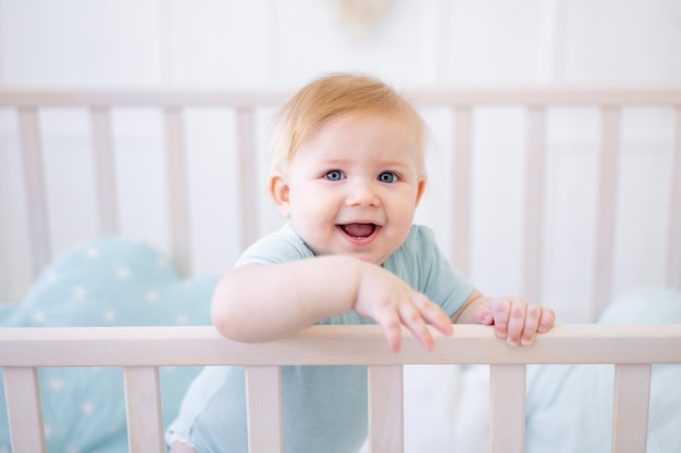 Closeup portrait of a small blonde baby smiling baby with blue eyes at home on the bed