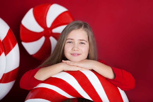 Closeup portrait of smiling little girl with big christmas candy on red background.