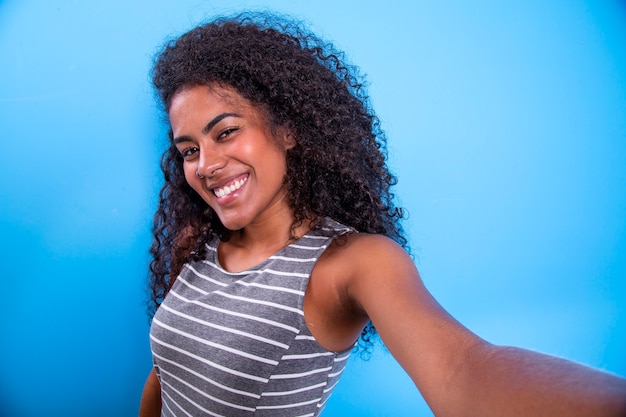 Closeup portrait of smiling young attractive African brazilian woman holding smartphone, taking selfie photo  