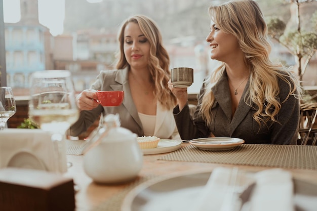 Closeup portrait of two female friends in strict suits laughing drinking coffee and wine on the