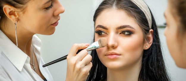 Closeup portrait of a woman applying dry cosmetic tonal foundation on the face using a makeup brush. Makeup detail.