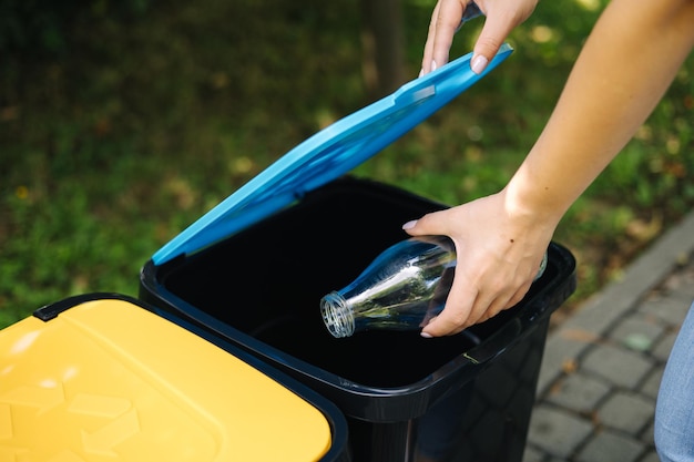 Closeup portrait woman hand throwig empty glass bottle in recycling bin different colour of plastic