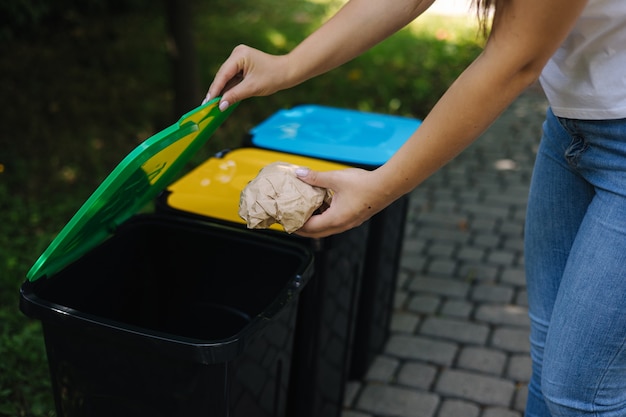 Closeup portrait woman hand throwing crumpled paper bag in recycling bin outdoors recycling bins