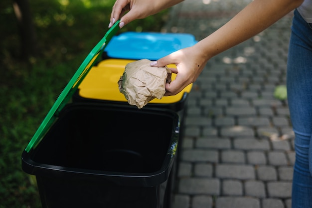 Closeup portrait woman hand throwing crumpled paper bag in recycling bin outdoors recycling bins