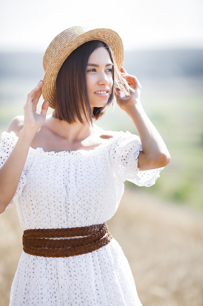 Closeup portrait of young beautiful woman outdoors on the meadow. Female in the hat on summertime. Lady in white dress.