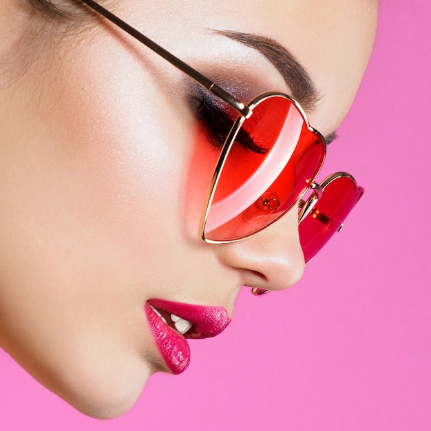 Closeup portrait of young beautiful woman red wearing heart shaped sunglasses. Smokey eyes and red lips