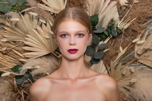 Closeup portrait of young beautiful woman with a healthy skin of the face. Blonde girl with burgundy lips against a background of spring dry field flowers. Beauty face care concept.