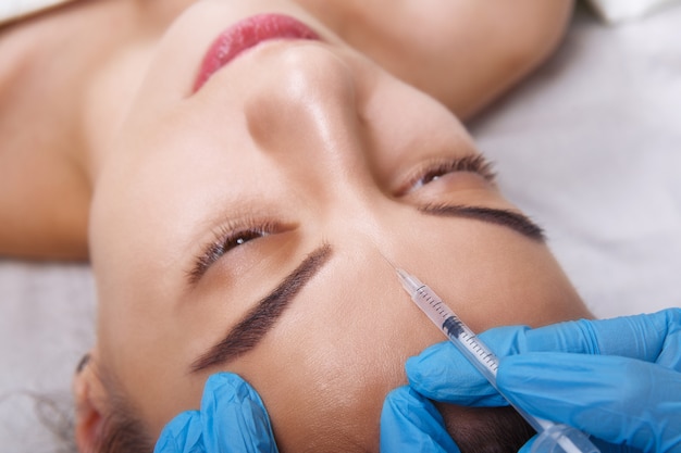 Closeup Portrait of young Caucasian woman getting cosmetic injection in forehead. People, cosmetology, plastic surgery and beauty concept.