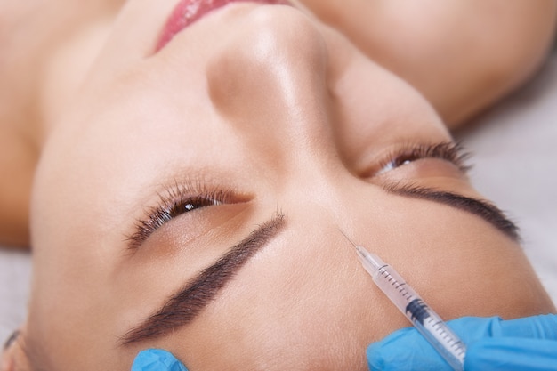 Closeup Portrait of young Caucasian woman getting cosmetic injection in forehead. People, cosmetology, plastic surgery and beauty concept.