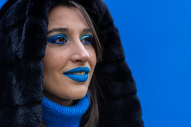 Closeup portrait of a young woman with blue makeup on a blue background