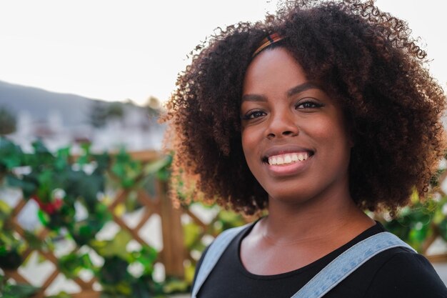 Closeup portrait of young woman with curly hair and African American features smiling outdoors Concept lifestyle curly hair