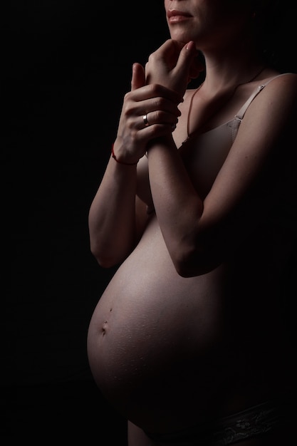 Closeup pregnant girl in a white tshirt hugs her belly with a baby