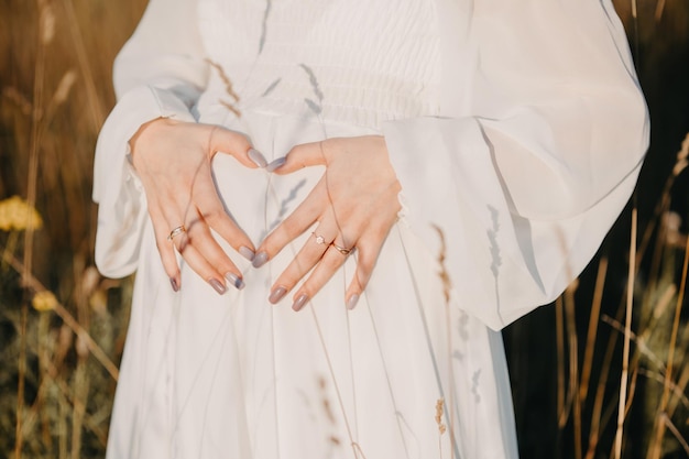 Closeup of pregnant woman with hands on her belly on nature background Silhouette of pregnant woman in white dress in sunlight of sunset Concept of pregnancy maternity expectation for baby birth